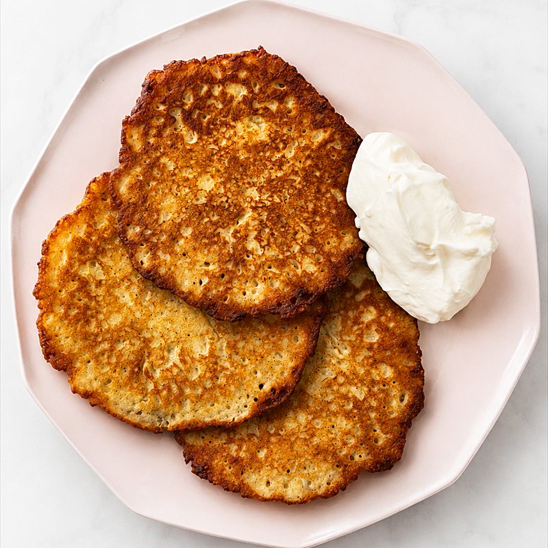 Three golden potato pancakes served with a spoon of sour cream.